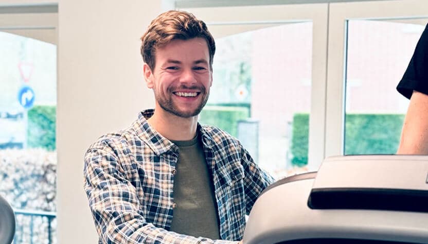 Man in a checkered shirt smiling while standing on a treadmill.