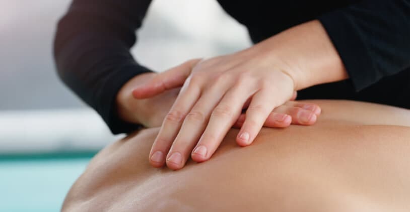 Close-up van handen die een massage geven op de rug van een patiënt.